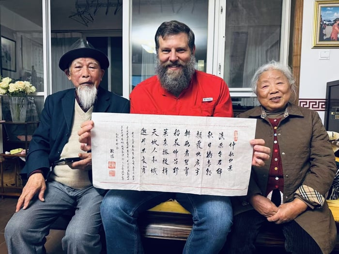 Bobby Robbins holding a calligraphy scroll with an elderly couple