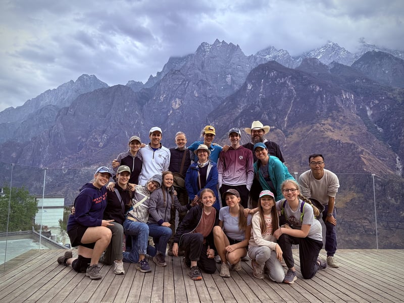 A smiling group posed on a deck below the peaks of Tiger Leaping Gorge