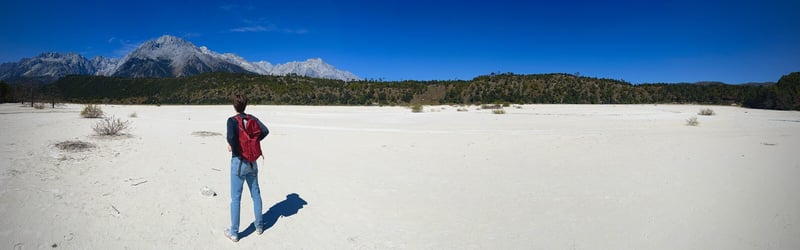 A traveler standing on the pale bed of Milky Lake below Jade Dragon Snow Mountain