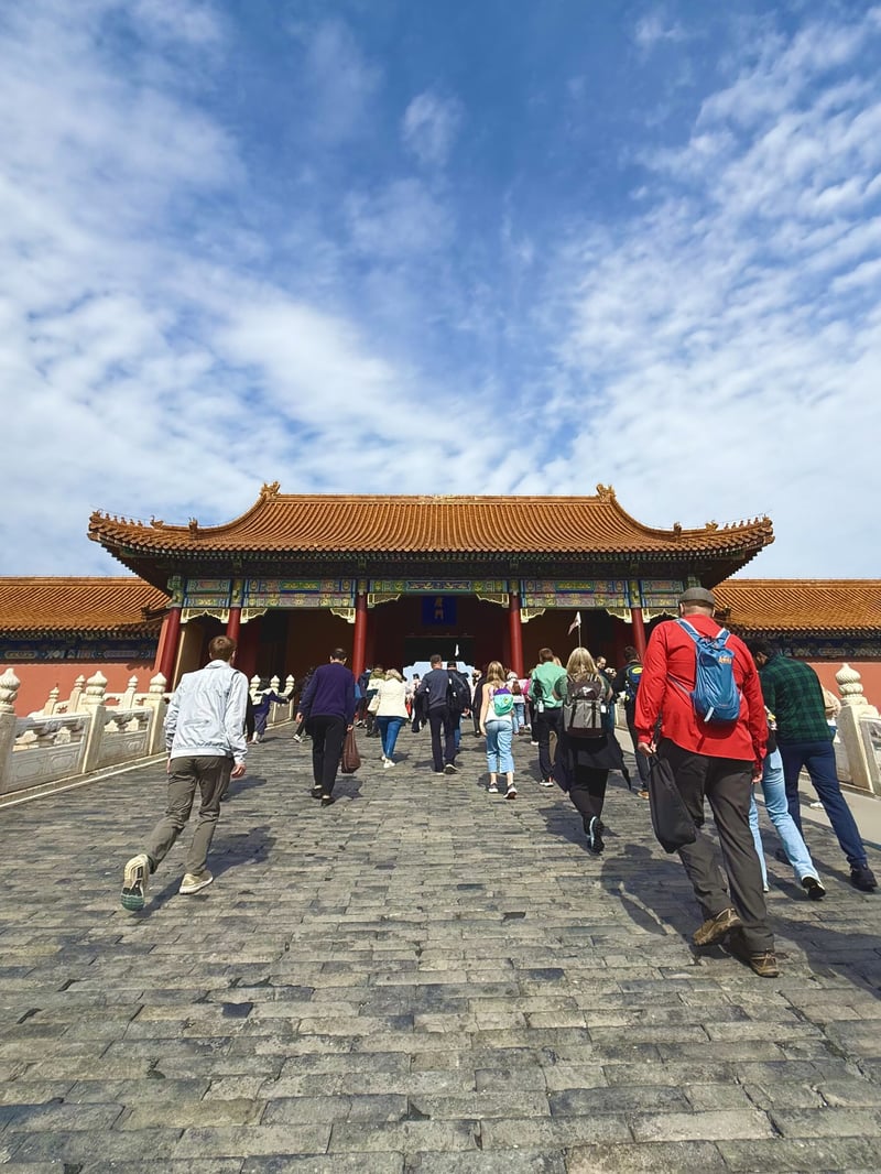 Travelers walking into the Forbidden City under a blue sky