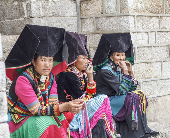 Yi women in traditional dress talking on a stone step